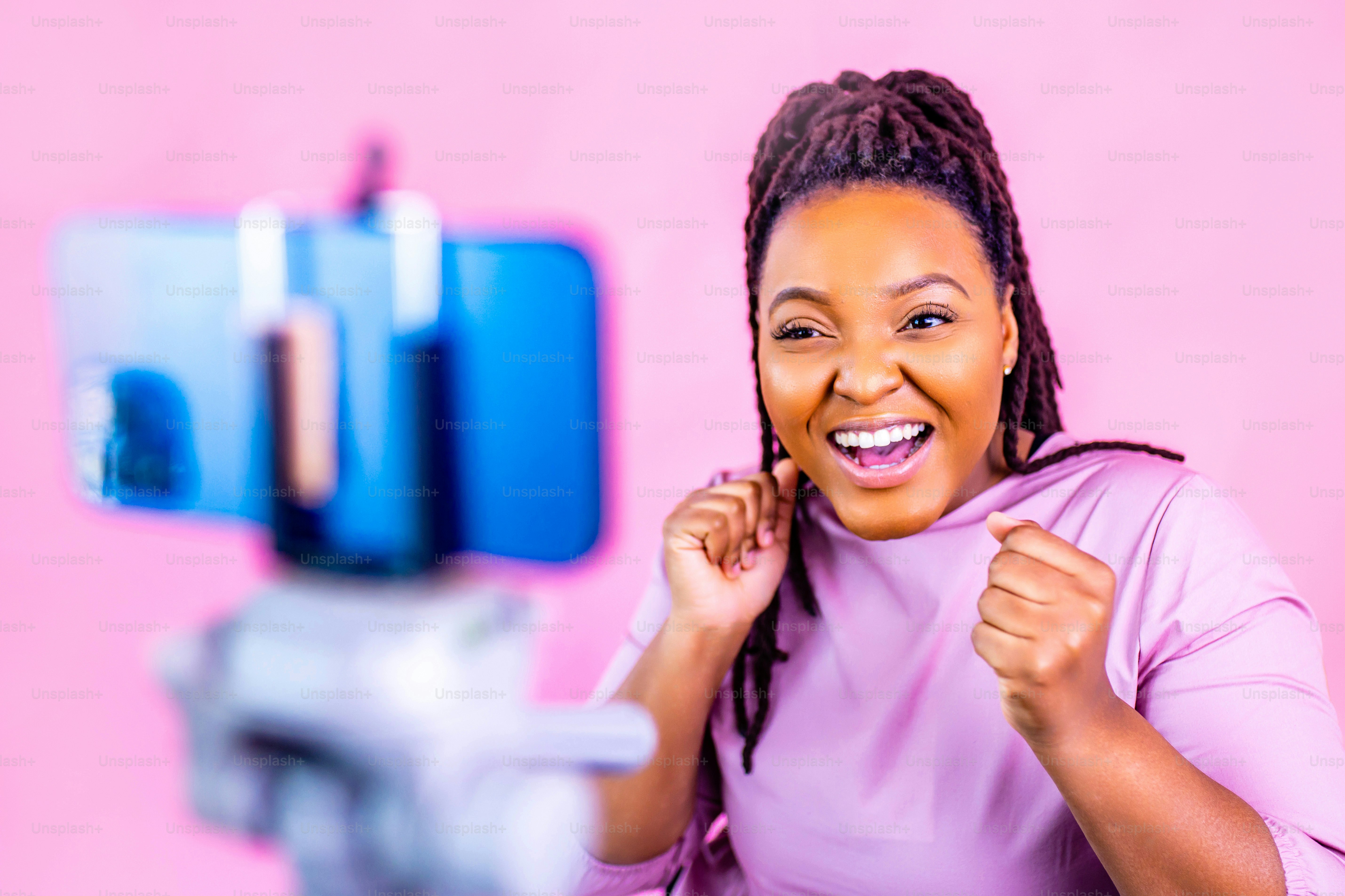 hispanic woman with cool dreadlocks pigtails wear pink dress in studio chatting with her subscribers by phone camera .